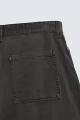 Pantalón de corte relaxed fit confeccionado en algodón, color gris oscuro. Presenta bolsillos delanteros, bolsillos laterales tipo cargo en las perneras y cierre frontal con cremallera y botón.