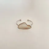 Pulsera plateada rígida con abertura, con pieza central de nácar irregular.