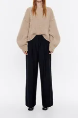 Pantalón negro de corte ancho y tiro alto, con cintura elástica fruncida y pliegues frontales.