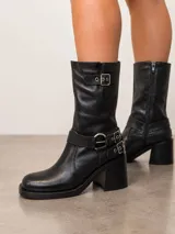 Bota biker de cuero color marrón, con diseño de caña media, punta cuadrada y taco cuadrado. Presenta detalles de correas con hebillas metálicas en el tobillo y en la parte superior de la caña.