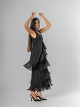 Vestido largo negro de seda con escote en V adornado con lentejuelas plateadas. Presenta un diseño de capas superpuestas con terminaciones deshilachadas que aportan volumen y movimiento. Es de corte sin mangas con breteles anchos y espalda elastizada.