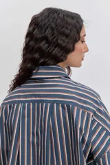 Camisa de corte oversize con diseño de rayas verticales en tonos azul y blanco, cuello clásico, cierre frontal con botones y mangas largas con puños abotonados.
