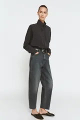 Jeans de tiro alto con corte barrel y diseño tapered, confeccionados en denim con efecto lavado y detalle de raya planchada. Presentan cintura con trabillas, cierre frontal con cremallera y botón, y bolsillos funcionales en delantero y espalda.