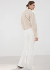 Jeans blancos de tiro alto y estilo flare, confeccionados en tejido elástico de algodón. Presentan diseño de cinco bolsillos, trabillas para cinturón y cierre frontal con cremallera y botón.