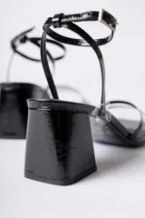Sandalias de tacón cuadrado medio, color negro con acabado brillante, diseño de tiras finas en el empeine y cierre de pulsera con hebilla al tobillo.