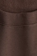 Buzo de tejido de punto color marrón oscuro, con cuello redondo, hombros caídos y puños y bajo acanalados. Presenta un estampado frontal en color crema con el texto "CHARME DE PARIS 1998".