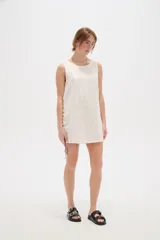 Vestido corto de algodón color blanco, de corte holgado, sin mangas y con cuello a la base. Presenta detalles de cordones cruzados y ojalillos en los laterales.