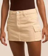 Pollera corta de sarga color beige claro, con cintura con trabillas y cierre de botón y cremallera. Presenta bolsillos cargo funcionales a los lados.