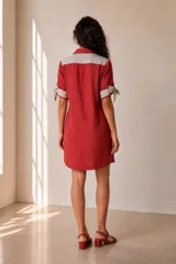 Vestido corto de lino color beige, de corte recto y holgado, con cuello polo y cierre frontal parcial con botones. Las mangas cortas cuentan con detalles de tiras para anudar en los puños.