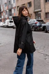 Parka liviana color beige con capucha, cierre frontal con botones, bolsillos delanteros con tapa y ajuste en la cintura. Presenta mangas con puños vueltos y detalle de botones.