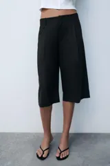 Bermuda de tiro medio color negro con bolsillos en el delantero y detalle de pinzas. Cuenta con cierre frontal con cremallera y ganchos metálicos.
