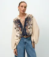 Blusa tipo bata de viscosa con estampa floral estilo paisley. Presenta cuello alto con detalle de volados, cierre frontal con botones y lazo ajustable en el escote. Posee mangas largas abullonadas con puños elásticos.