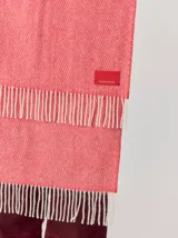 Bufanda de gran tamaño en color mostaza con diseño de tejido en espiga y flecos en los extremos. Incluye una etiqueta metálica decorativa en una de las esquinas.