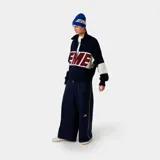 Campera de punto azul marino con cierre frontal, cuello polo y mangas largas con franjas horizontales blancas. Presenta la palabra 'EME' en color rojo en el pecho.