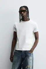 Camiseta de corte relajado, color gris claro, confeccionada en tejido con estructura waffle. Presenta cuello redondo y manga corta, con costuras decorativas en contraste color dorado que recorren los laterales y los hombros.