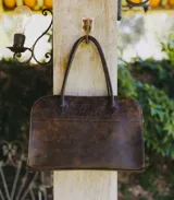 Bolso tipo tote de cuero negro con textura tipo piel de cocodrilo, doble asa de mano y cierre superior con cremallera.