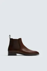 Bota estilo chelsea de cuero color marrón, con paneles elásticos laterales, tirador trasero y horma en punta con suela de tacón bajo.