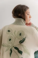 Saco tejido tipo jacquard color bordó con diseño floral en la espalda, cuello alto y cierre frontal de aluminio. Presenta detalles en azul y blanco en el cuello, puños y ruedo, con un patrón geométrico de rombos en la parte inferior.