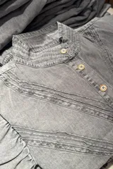 Camisa gris de jean liviano con cuello mao, cierre frontal con botones dorados, mangas 3/4 con puños fruncidos y detalle de costuras horizontales en el pecho.
