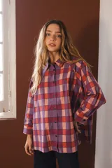 Camisa de corte oversize con estampado de cuadros en tonos violeta, rojo y rosa. Presenta cuello clásico, cierre frontal con botones y detalle de bordado pequeño en el pecho. Cuenta con cierre de botones en los laterales.