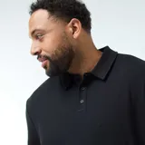 Polo negro de manga corta con cuello y tapeta de tres botones. El tejido presenta una textura de punto waffle o piqué sutil.