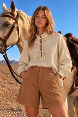Blusa blanca de manga larga con cuello alto y volados, cierre frontal con lazos y diseño holgado.