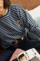 Remerón de manga larga y tejido de punto, con diseño de rayas finas horizontales en tonos rojos y rosados. Presenta cuello redondo y logo bordado a mano en el pecho.
