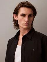 Camisa negra de manga larga con cuello abotonado y logo de Calvin Klein bordado en el pecho.