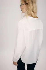 Camisa amplia de cuello solapa con escote en pico y manga larga, en tejido satinado de color bordó. Cuenta con un bolsillo de plastrón en el frente y un diseño holgado.