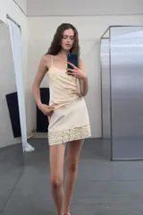 Falda mini de tiro medio en color crudo, con detalle de volantes en el ruedo adornados con tachas metálicas. Cuenta con cierre lateral oculto.