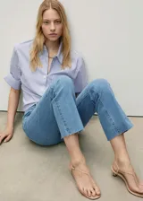 Jeans flare tiro medio color azul claro, con diseño crop y bajo deshilachado. Cuenta con presillas para cinturón, cierre frontal de cremallera y botón, y clásico diseño de cinco bolsillos.