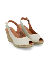 Sandalia de cuero napa color crema, tipo alpargata con cuña de yute, punta cerrada y tira ajustable al tobillo con hebilla.