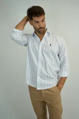 Camisa de manga larga con estampado de rayas verticales en color celeste sobre fondo blanco. Presenta cuello clásico, cierre frontal con botones y bordado pequeño en el pecho.