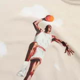 Remera de algodón color beige con estampado integral de nubes y gráfico central de Michael Jordan en pleno salto.