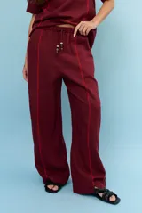 Pantalon de lino color marrón con costuras blancas decorativas a lo largo de las piernas y corte amplio.