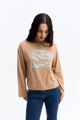 Remera de manga larga color beige, con cuello redondo y estampa gráfica frontal en color celeste.