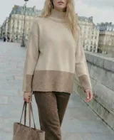 Sweater tipo polera de calce oversize, con diseño color block que combina tonos beige y marrón. Presenta cuello alto, mangas largas con puños acanalados y un panel inferior acanalado a juego.