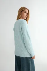 Buzo de tejido de punto con textura suave, color celeste pastel con efecto jaspeado. Presenta cuello redondo, mangas largas con terminación en puño y un diseño de canalé en la parte superior del pecho.