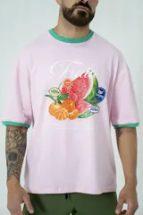 Remera oversize rosa con cuello y mangas con ribete verde. Estampado frontal con diseño de frutas y texto.