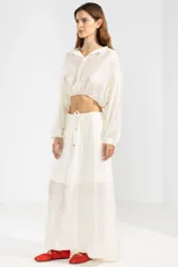 Camisa cropped de manga larga confeccionada en crepé color crema, con cuello camisero, botones frontales y elástico en la cintura.