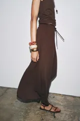 Falda larga de tiro medio, color beige claro, con caída amplia y cinturón fino negro anudado en la cintura.