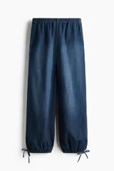 Pantalón tobillero en denim suave de corte holgado con piernas globo, cintura elástica y bolsillos laterales discretos, con abertura ajustable mediante cordón en los bajos.