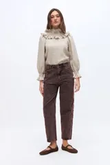 Blusa de lino color beige, con cuello alto fruncido y detalles de volados en el cuello y los puños elásticos. Presenta mangas largas abullonadas y diseño holgado.