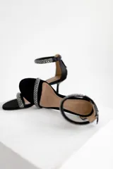 Sandalias de tacón alto negras con tiras adornadas con pedrería brillante. Tienen una tira en la parte delantera del pie y otra alrededor del tobillo con cierre de cremallera en la parte trasera.