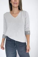 Sweater de tejido de punto color gris, con escote en V y mangas largas. Presenta un diseño liso en el exterior y un detalle de animal print en el interior de los puños, visible al doblarlos.