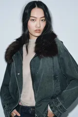 Chaqueta tipo bomber de denim lavado azul, corte holgado, con cuello solapa y aplicación de pelo sintético marrón desmontable. Presenta bolsillos delanteros y bajo acabado en elástico.