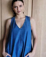 Vestido largo de denim azul, con escote en V, sin mangas, corte holgado, bolsillos laterales y aberturas en los costados de la falda.