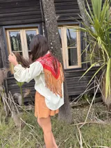 Camisa de jean con diseño estilo western, featuring un canesú trasero con estampado paisley en blanco y azul, y flecos largos de cuero rojo. Cuenta con mangas largas abullonadas con puños elásticos fruncidos.