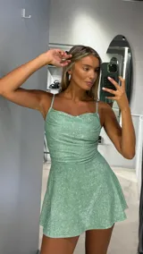 Vestido corto verde menta con brillos, escote drapeado, tirantes finos y falda acampanada.