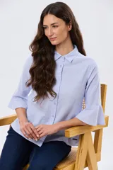 Camisa de lino celeste con cuello clásico, cierre frontal con botones y mangas tres cuartos terminadas en volados.